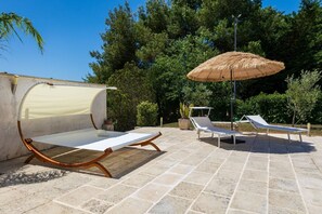 Een terras met een ligbed, een tafel met zonnescherm en een grote parasol.