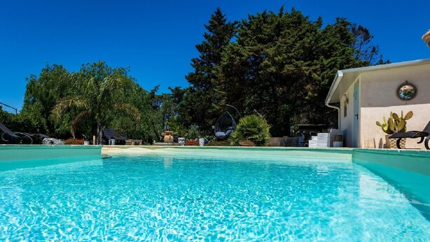 Piscina azul cristalina rodeada de exuberante vegetación y un edificio con un ventanal circular.