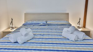 Habitación de hotel con una cama, dos mesitas de noche y dos toallas enrolladas sobre la cama.