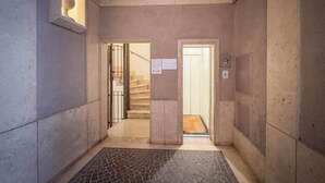 Ein Flur mit Fliesenboden, einer zur Treppe führenden Tür und einer Wandleuchte.