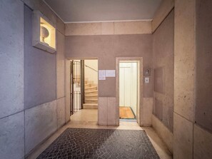 Ein Flur mit Fliesenboden, einer zur Treppe führenden Tür und einer Wandleuchte.