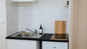 A compact kitchen with white cabinetry, a black countertop, and a small refrigerator. - L’Élégant Cocon • Terrasse • Versailles • Paris • Gare SQY (Montigny-le-Bretonneux)