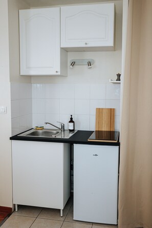 A compact kitchen with white cabinetry, a black countertop, and a small refrigerator. - L’Élégant Cocon • Terrasse • Versailles • Paris • Gare SQY (Montigny-le-Bretonneux)