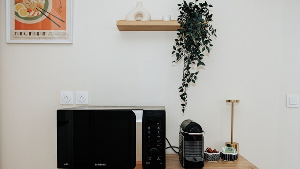 A kitchen area with a microwave, a coffee maker, and a wall-mounted shelf with a plant. - L’Élégant Cocon • Terrasse • Versailles • Paris • Gare SQY (Montigny-le-Bretonneux)