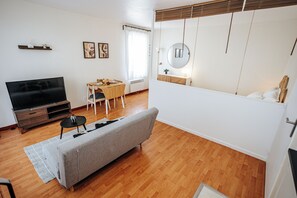 Ein modernes Wohnzimmer mit Sofa, Fernseher, Esstisch und einer kleinen Küchenzeile.