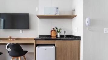 Une cuisine moderne équipée d’un four à micro-ondes, d’une machine à café, d’un petit réfrigérateur et d’une planche à découper en bois.