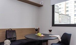 A room with a round table, two wine glasses, a plate with grapes and a macaron, a black bag, and a chair.