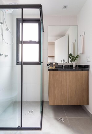 Een moderne badkamer met een douchecabine van glas, een houten wastafelmeubel en een grote spiegel.