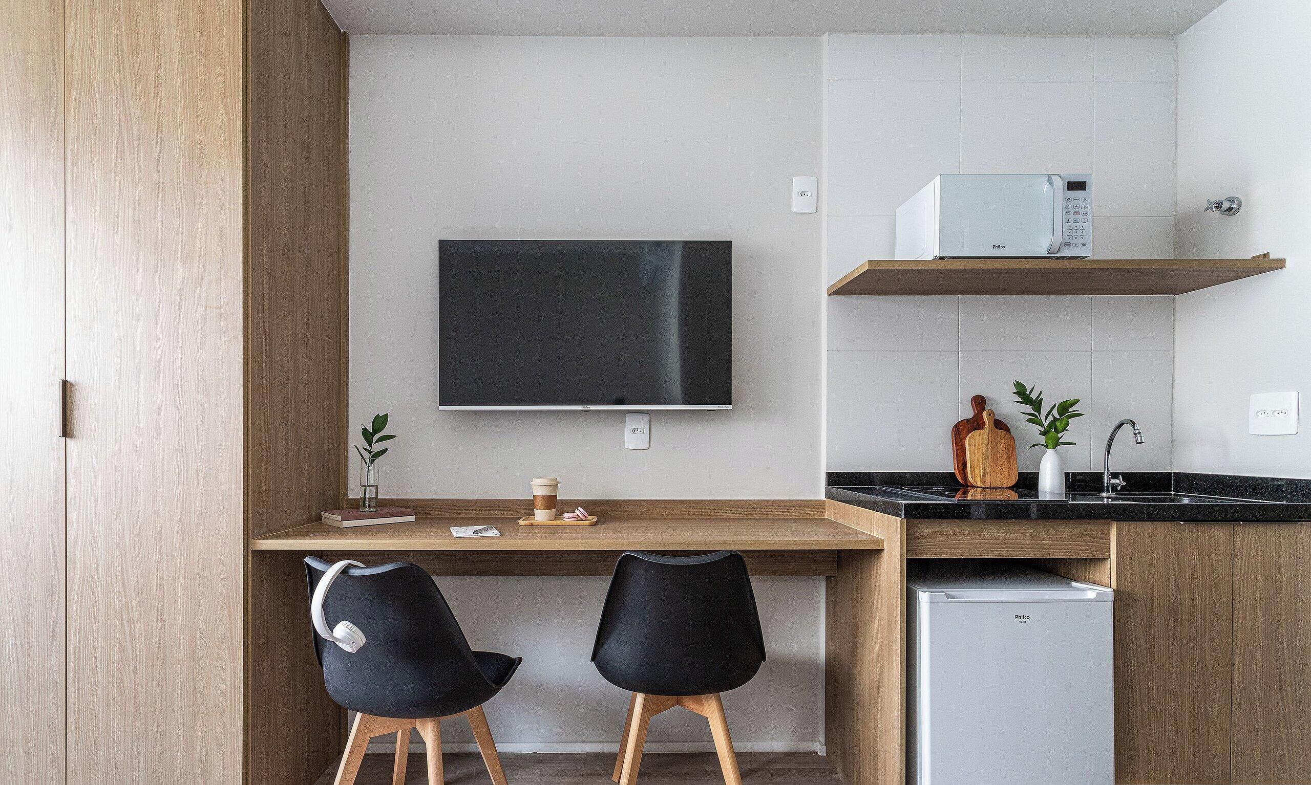 A modern kitchen with a flat-screen TV, a coffee machine, and a small refrigerator.