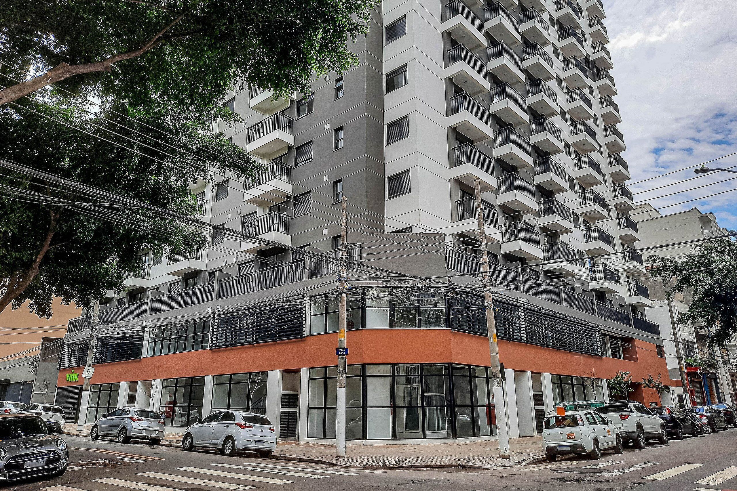 A multi-story building with balconies, a ground-level commercial space, and parked cars.