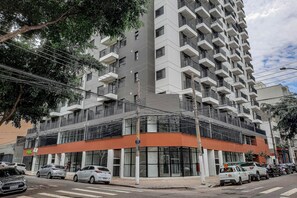 A multi-story building with balconies, a ground-level commercial space, and parked cars.