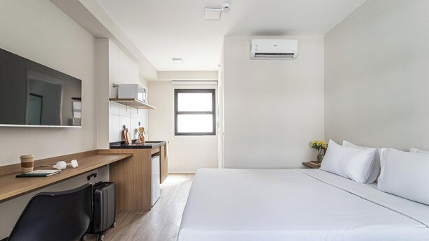 Une chambre d’hôtel moderne avec un grand lit, un bureau équipé d’un ordinateur, une chaise et une valise.