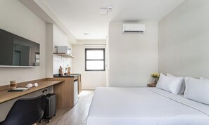 Une chambre d’hôtel comprenant un lit, un bureau avec un ordinateur, un four à micro-ondes, une petite kitchenette et une fenêtre.