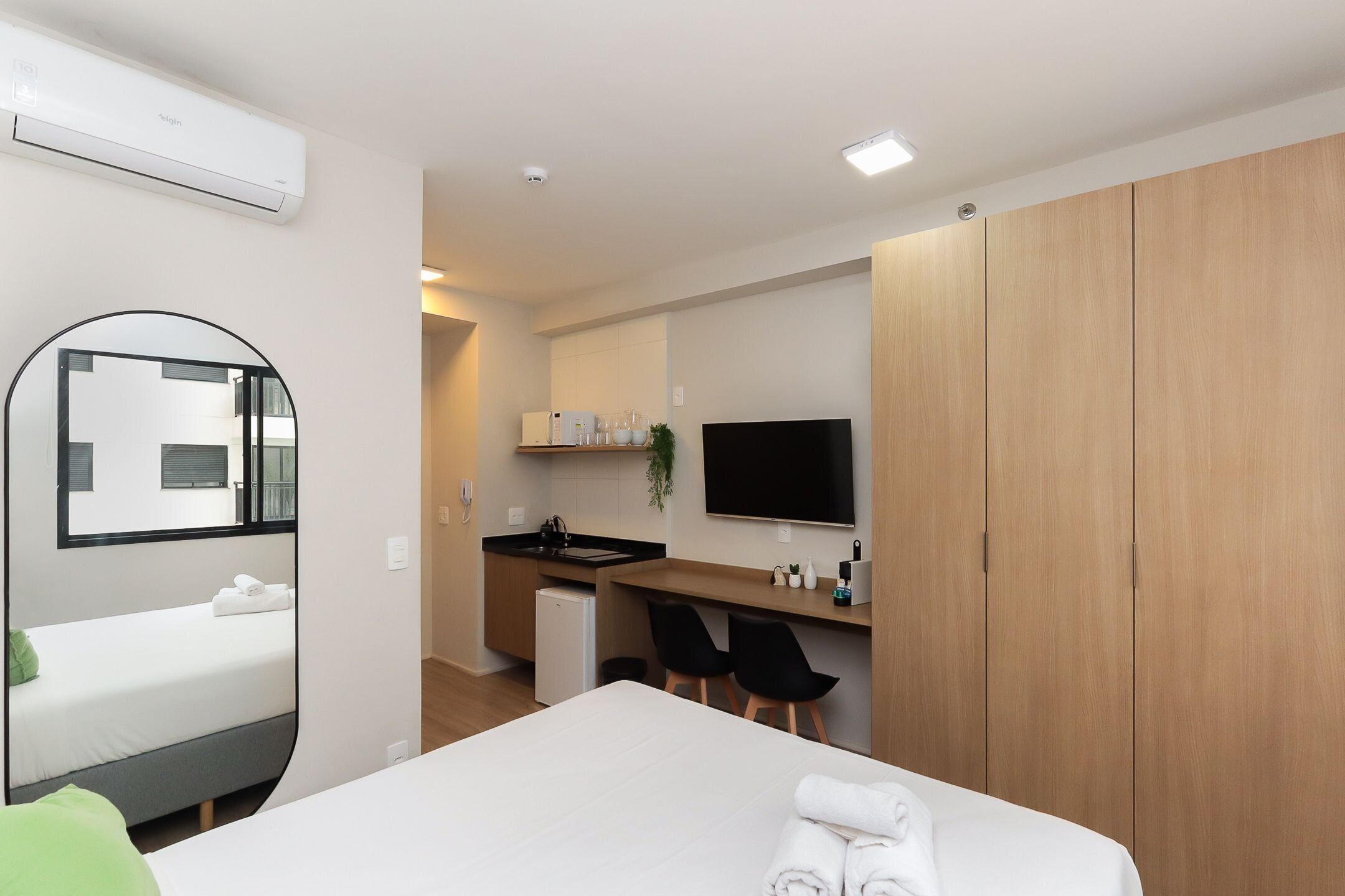 A hotel room with a bed, a desk with a chair, a television, and a wardrobe.
