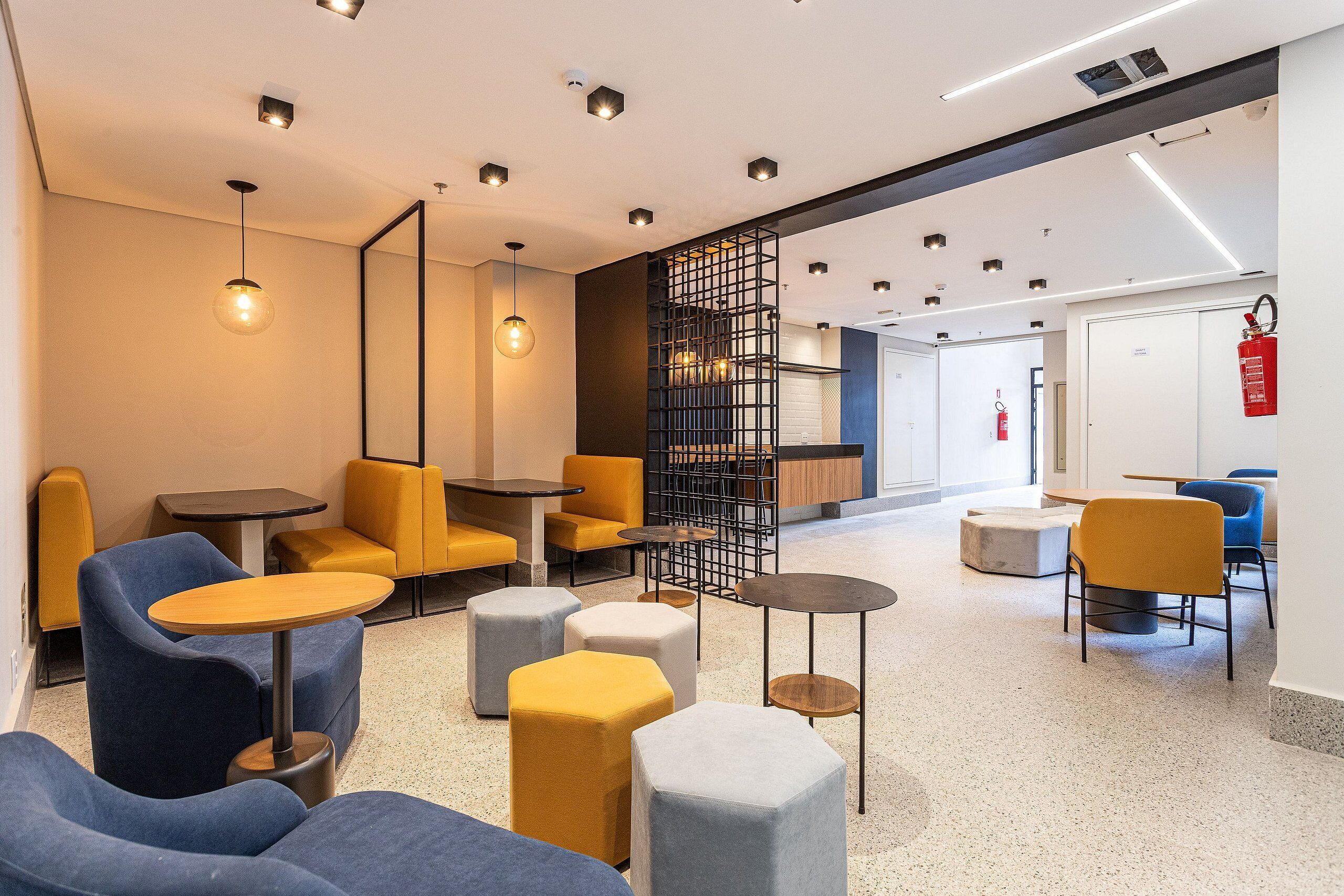 Een moderne lounge met zithoeken, tafels en een brandblusser aan de muur.
