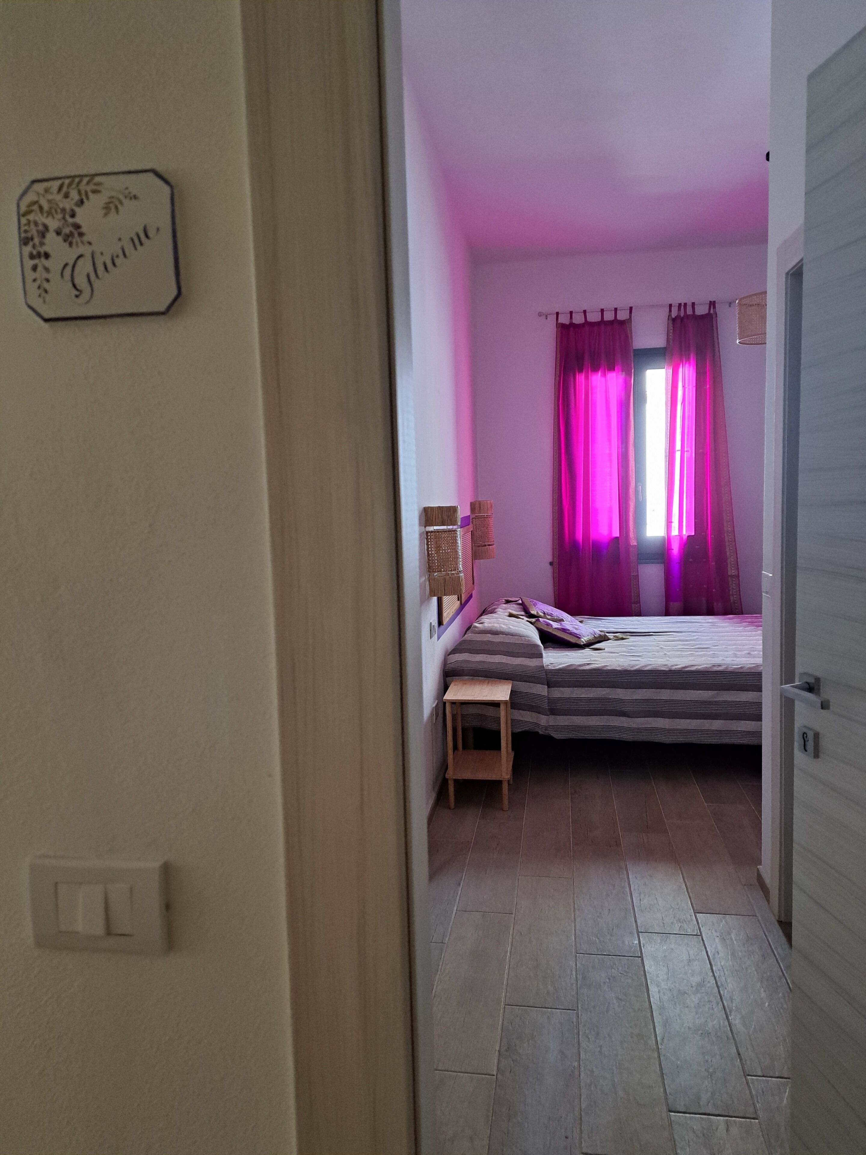 Un couloir étroit mène à une chambre à coucher qui contient un lit, une petite table et des rideaux.
