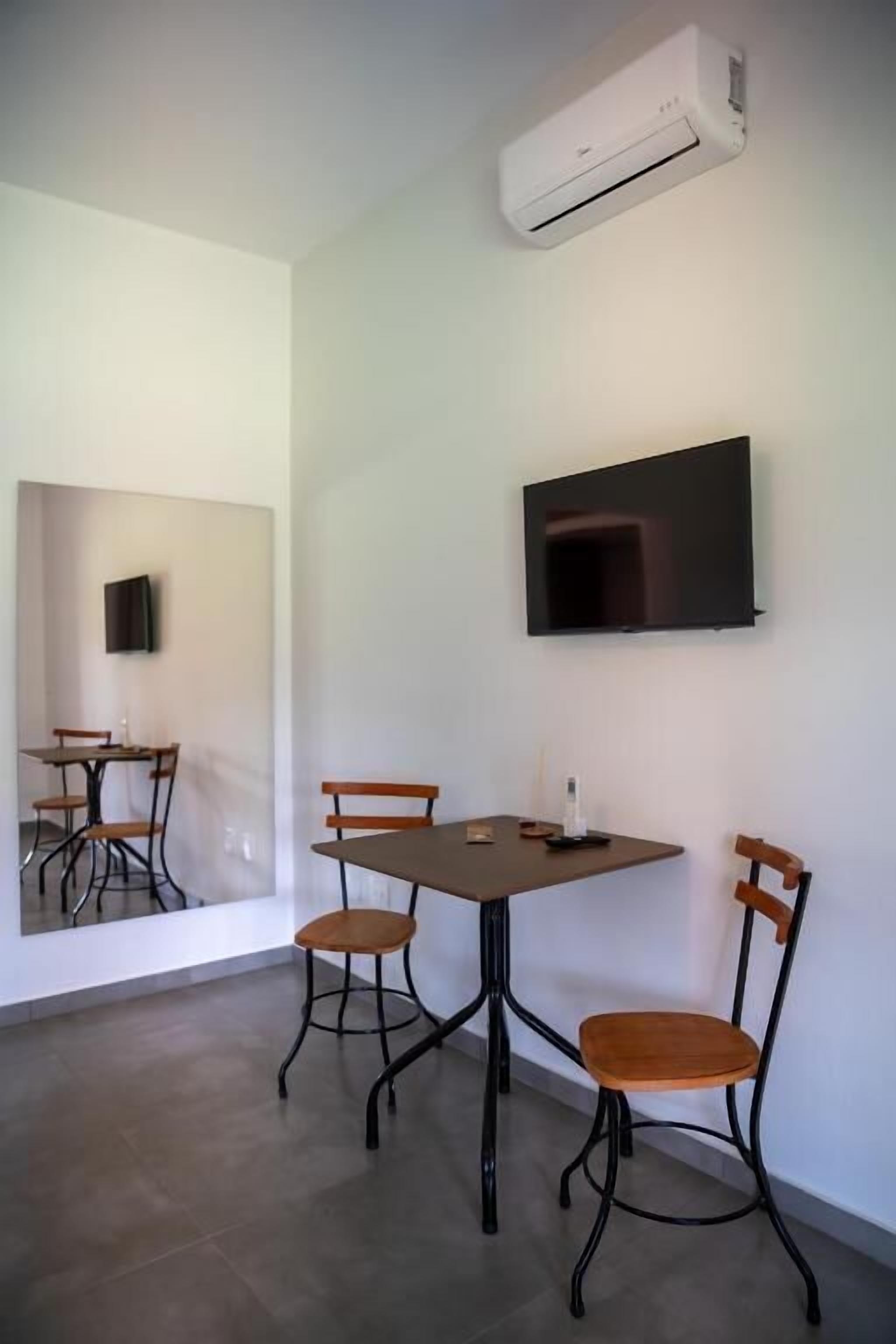Una habitación con una mesa de comedor, cuatro sillas, un televisor de pantalla plana en la pared y un equipo de aire acondicionado.