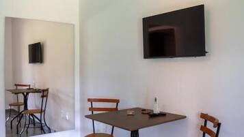Una habitación con una mesa de comedor, cuatro sillas, un televisor de pantalla plana en la pared y un equipo de aire acondicionado.