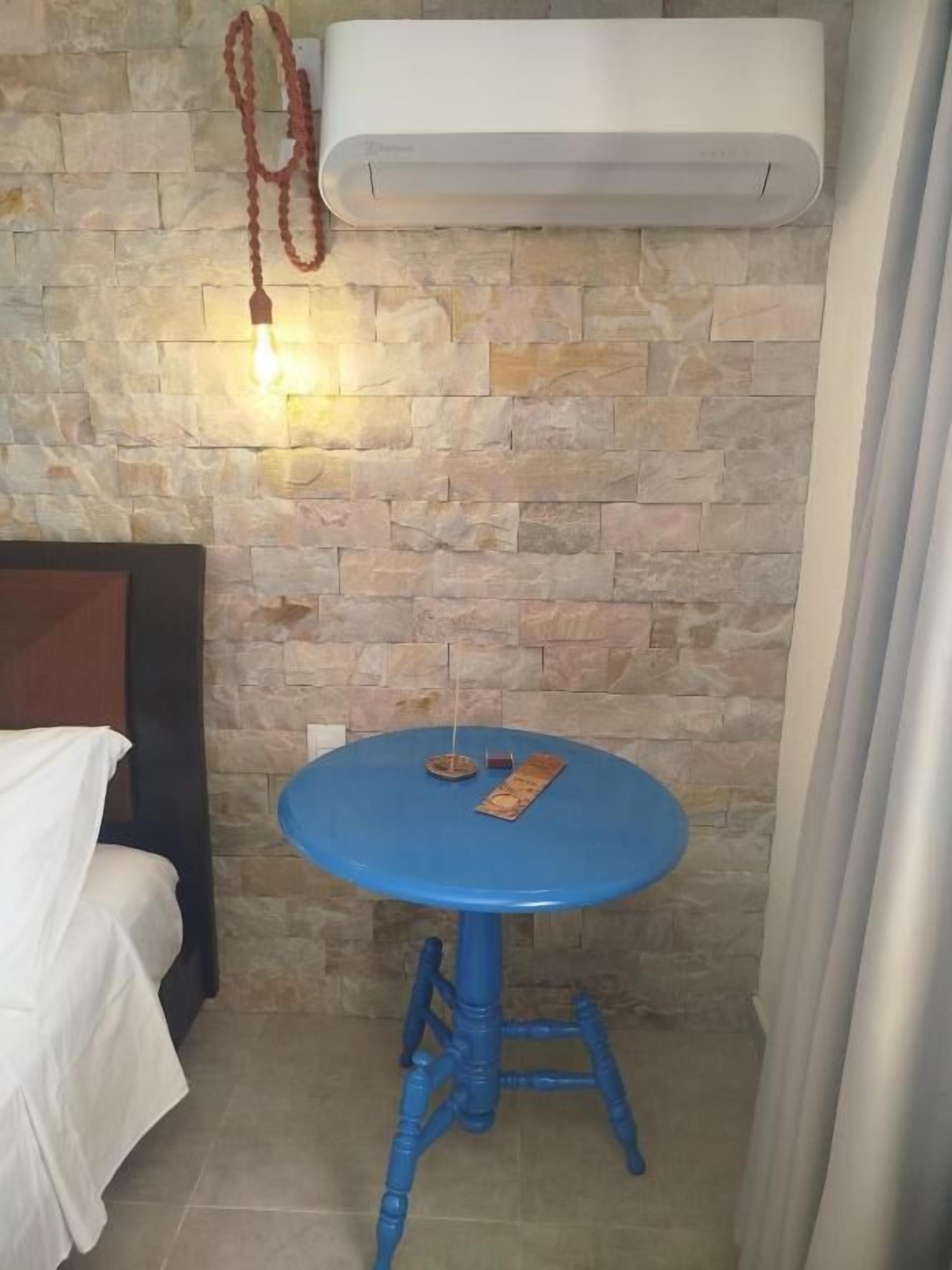 A room with a stone wall, a blue stool, a bed with a white cover, and an air conditioning unit.