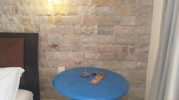 A room with a stone wall, a blue stool, a bed with a white cover, and an air conditioning unit.