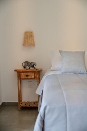 Un dormitorio con una cama, una mesita de noche con una lámpara y un adorno sobre la mesa.