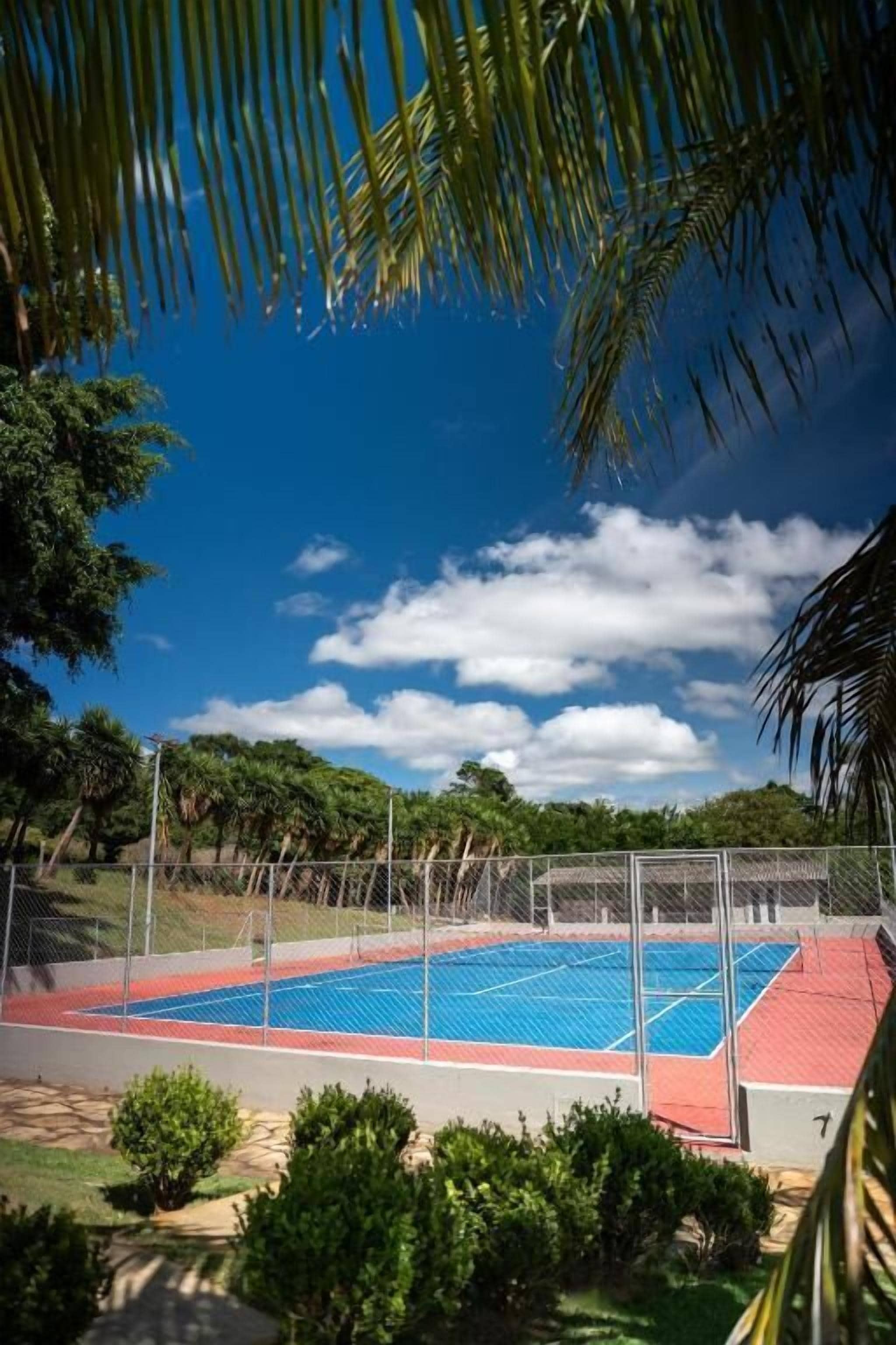 A tennis court with a fence, surrounded by greenery and trees.