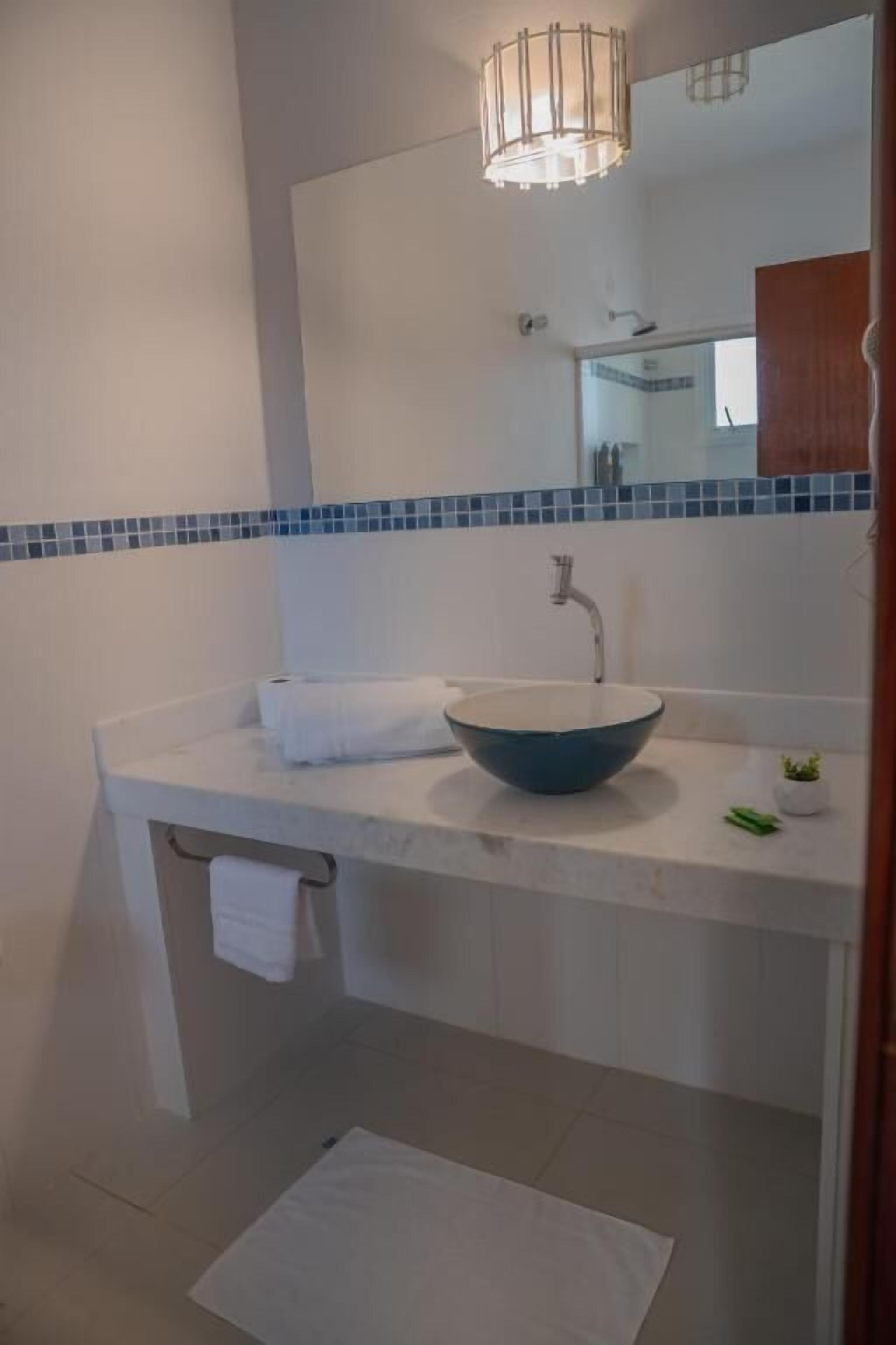 Un baño con encimera blanca, lavamanos azul, perchero y espejo.