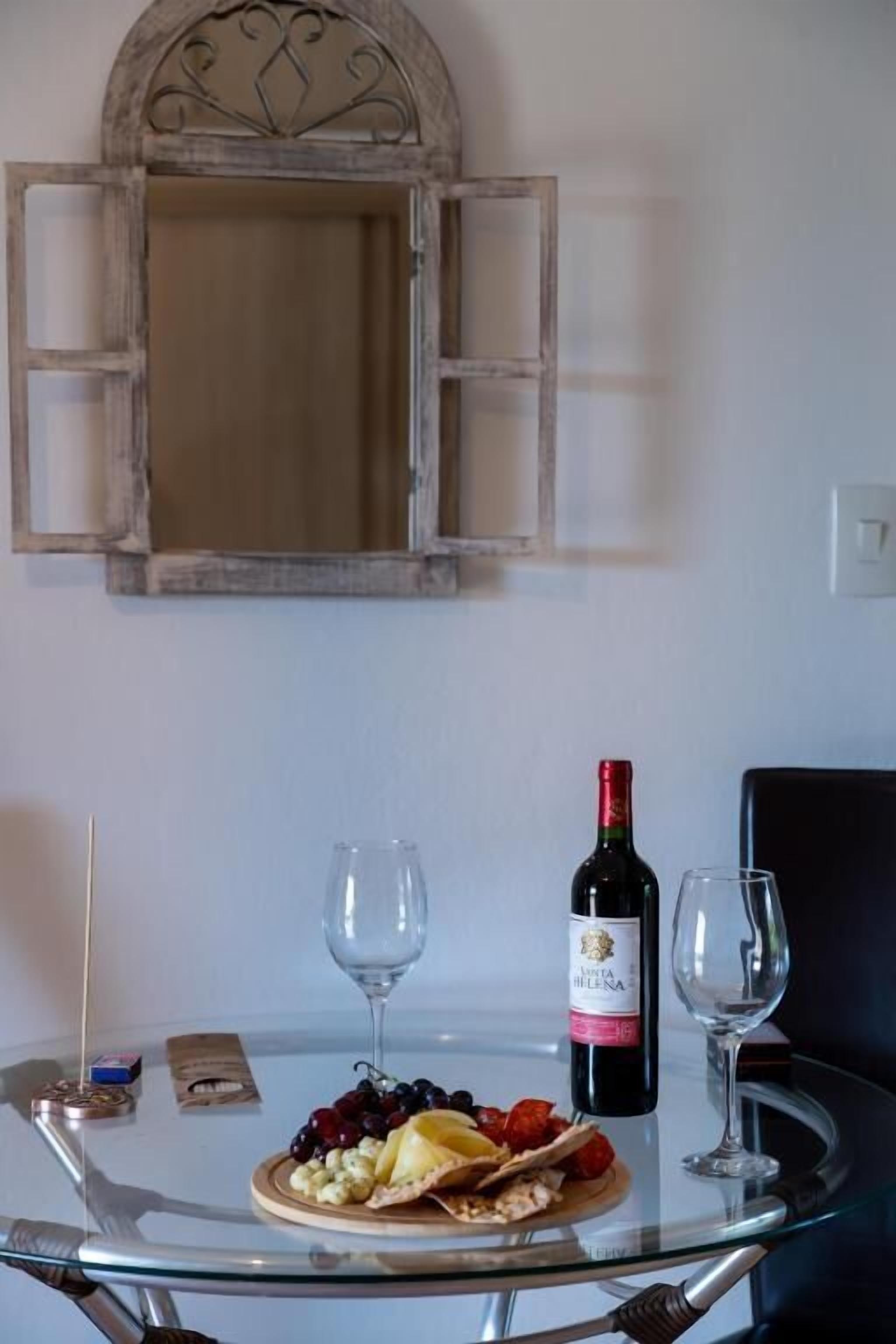 Une table en verre avec une bouteille de vin, deux verres et une assiette de fruits.