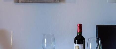 Une table en verre avec une bouteille de vin, deux verres et une assiette de fruits.