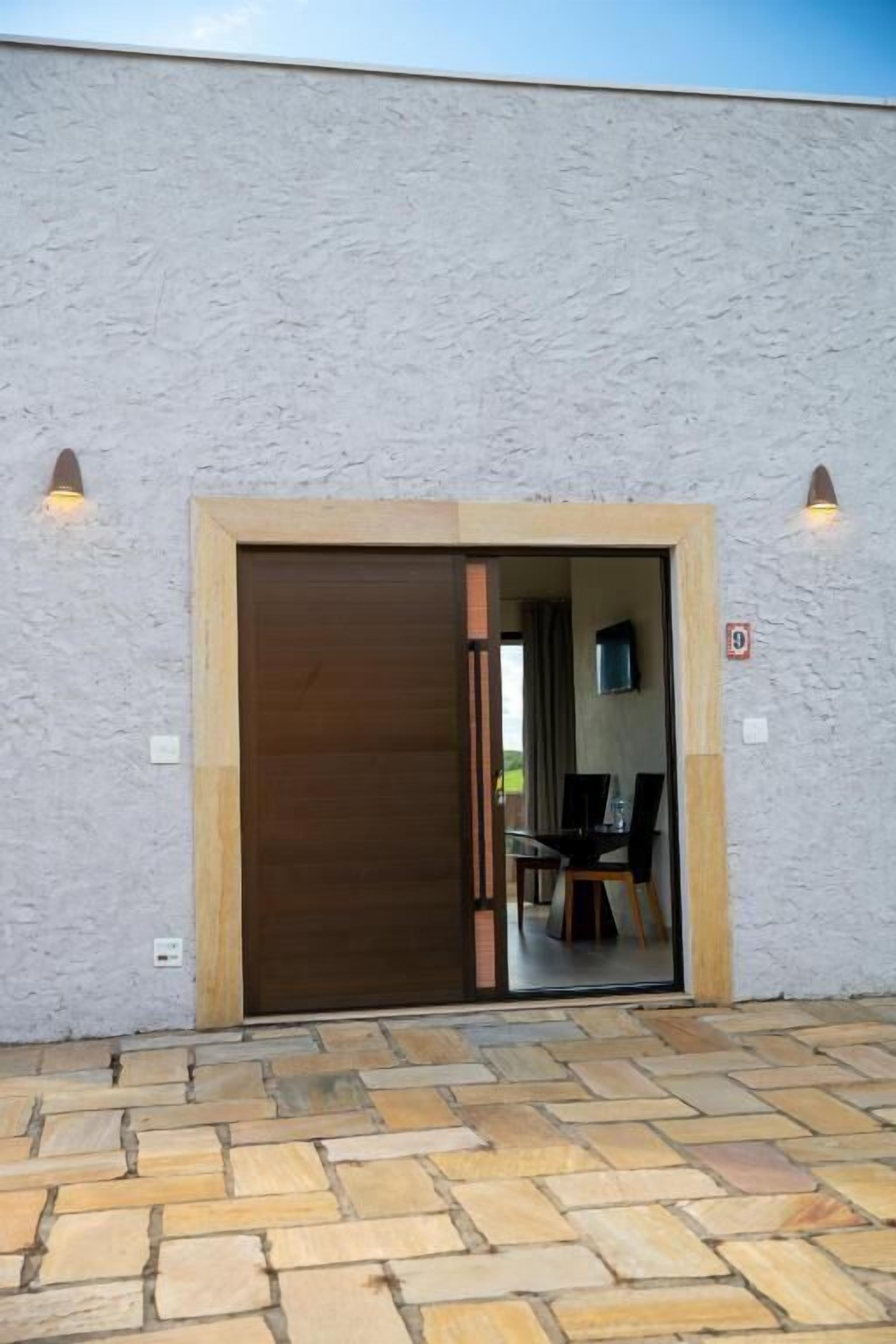 A building entrance with a sliding door, a paved patio, and two wall-mounted lights.