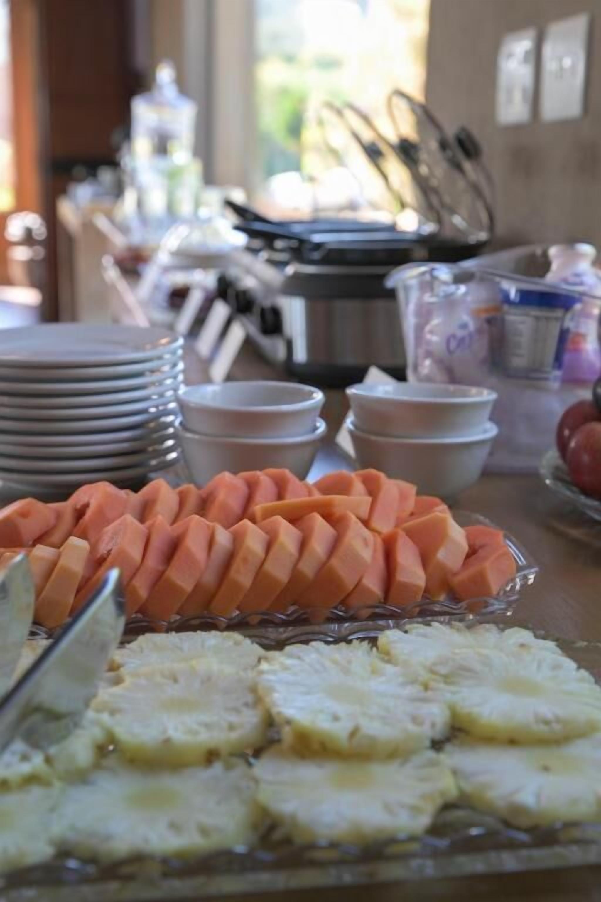 A buffet table with sliced fruits and vegetables, plates, and bowls.
