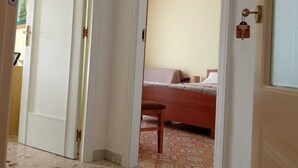 Un pasillo que conduce a un dormitorio con una cama, una silla y una puerta con cerradura de llave.