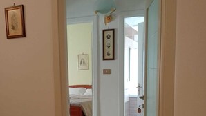 A narrow hallway leading to a bedroom with a bed and a door.