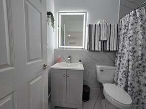 Ein Badezimmer mit Toilette, Waschbecken, Spiegel und einer Duschvorhang mit Blumenmuster.