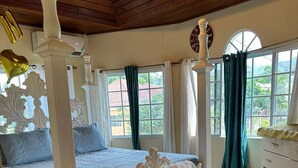A bedroom with a four-poster bed, a white dresser, and a view of the outside through large windows. - Cozy 3-bedroom house in serene Santa Cruz with AC (Santa Cruz)
