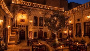 An outdoor courtyard with stone buildings, a central tree, and tables and chairs arranged for dining. - İNCİRLİ KONAK HOTEL (Şanlıurfa)