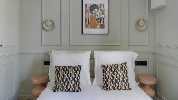 Une chambre d’hôtel comprenant un lit, deux tables de chevet, une œuvre d’art encadrée au-dessus du lit et un luminaire fixé au mur.