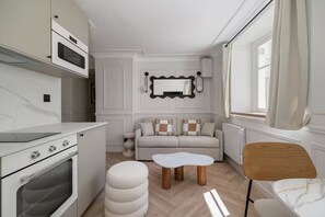 Ett modernt kök med vita skåp, en inbyggd ugn och en matplats med ett vitt bord och trästolar.