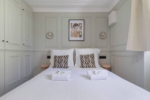 Ett hotellrum med en stor säng, två kuddar, två sängbord, en inramad tavla på väggen och ett fönster med gardiner.