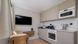 A compact kitchen with a built-in oven, microwave, and a flat-screen TV mounted on the wall.