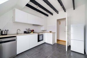 A modern kitchen with white cabinetry, a dishwasher, an oven, and a refrigerator. - Charming Flat near Madeleine (Paris)
