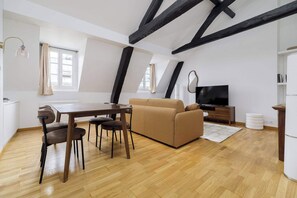 A loft-style room with a dining table, sofa, TV, and wooden beams. - Charming Flat near Madeleine (Paris)