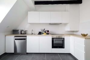 A modern kitchen with white cabinetry, a dishwasher, an oven, a microwave, and a toaster. - Charming Flat near Madeleine (Paris)