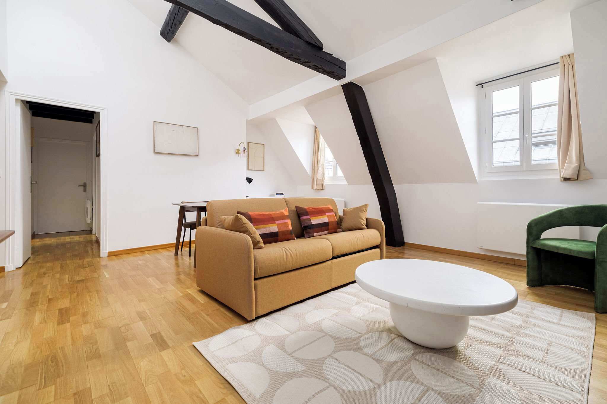 Ein modernes Loft-Zimmer mit Holzboden, einem beigefarbenen Sofa mit bunten Kissen, einem weißen Couchtisch und einem grünen Sessel.