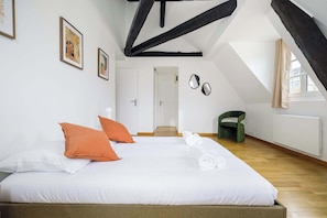 A bedroom with a bed, pillows, a rolled-up towel, a green chair, and a door. - Charming Flat near Madeleine (Paris)