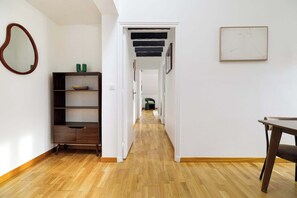 A hallway with wooden flooring, a bookshelf, a mirror, and a table. - Charming Flat near Madeleine (Paris)