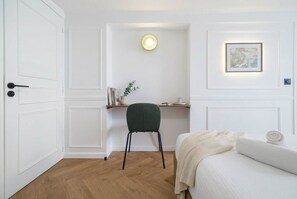 Ein Zimmer mit einem Bett, einem Schreibtisch mit Stuhl, einer Wandleuchte und einem gerahmten Bild.