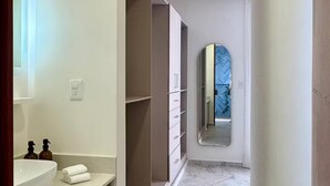 Un pasillo estrecho con un baño a la izquierda, que incluye un lavabo y un perchero para toallas.