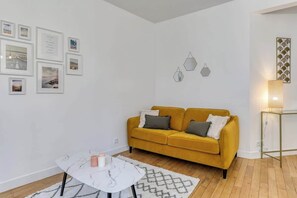 Ein Wohnzimmer mit einem gelben Sofa, einem weißen Couchtisch und gerahmten Bildern an der Wand.