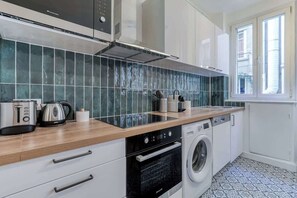 A modern kitchen with a wooden countertop, stainless steel appliances, and a built-in washing machine. - Poissonnière – Cosy Apartment near Montmartre (Paris)